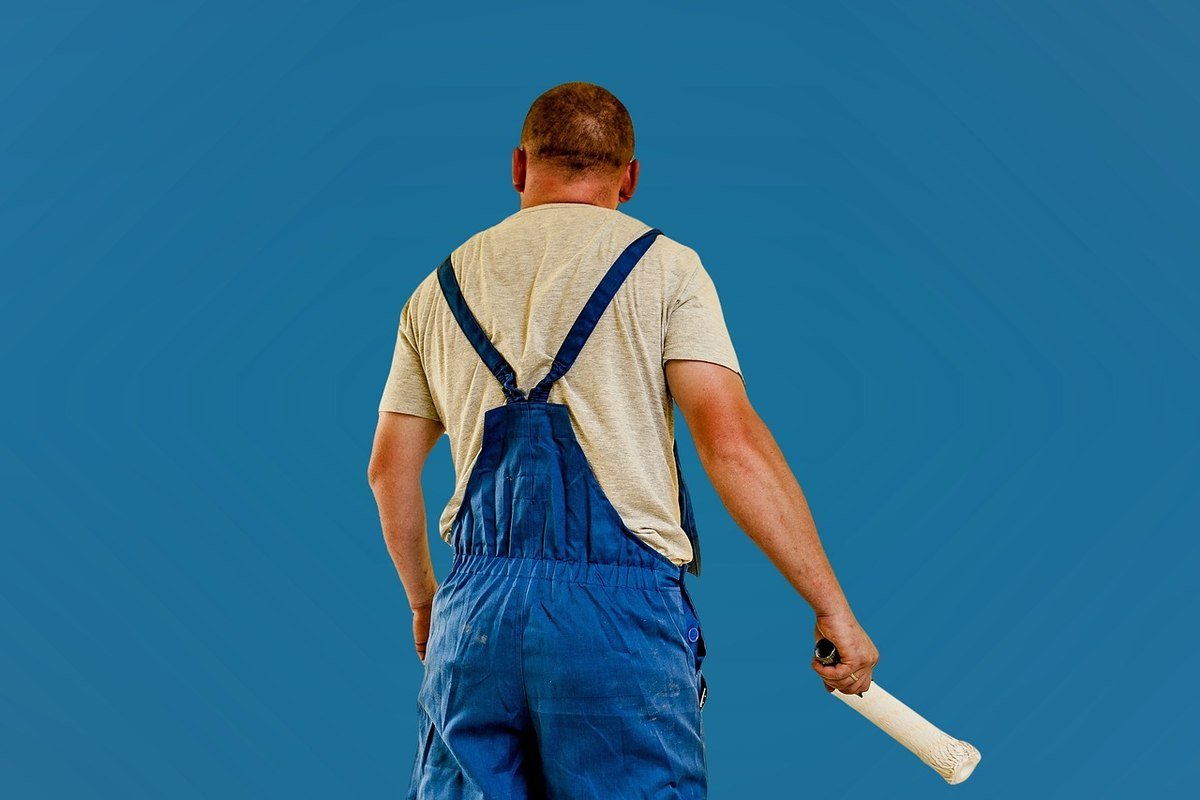 Homme en overalls bleus et t-shirt blanc, rouleau à la main, contre fond bleu