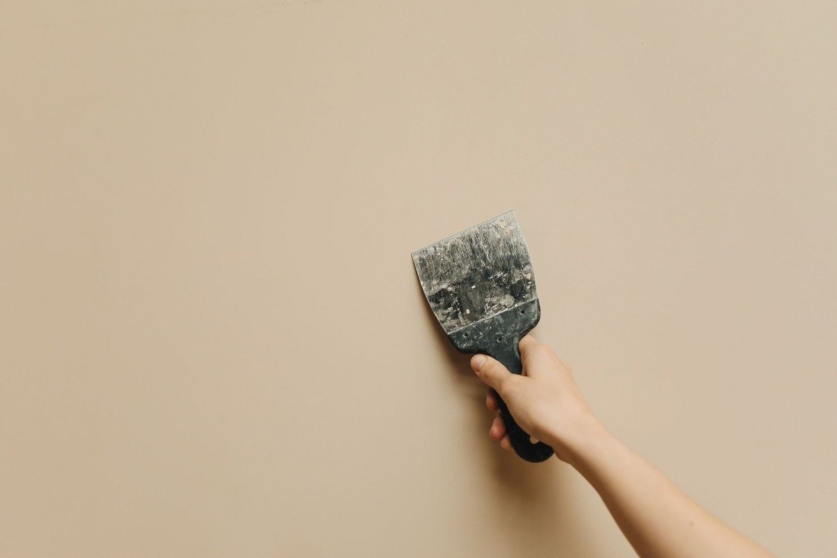 Une main tient un couteau à enduire contre un mur clair