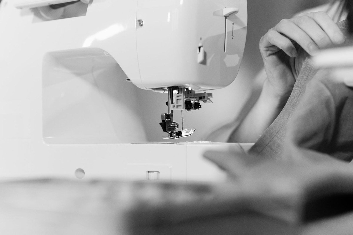 Machine à coudre blanche en action sur un tissu, mains visibles Machine à coudre blanche en action sur un tissu, mains visibles